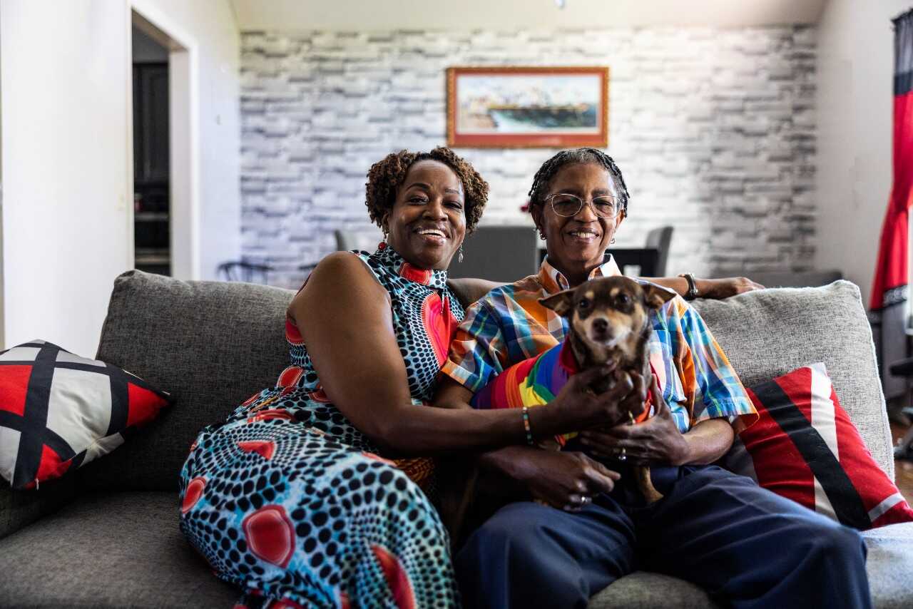 Lesbian couple embracing on couch in their living room with their dog 